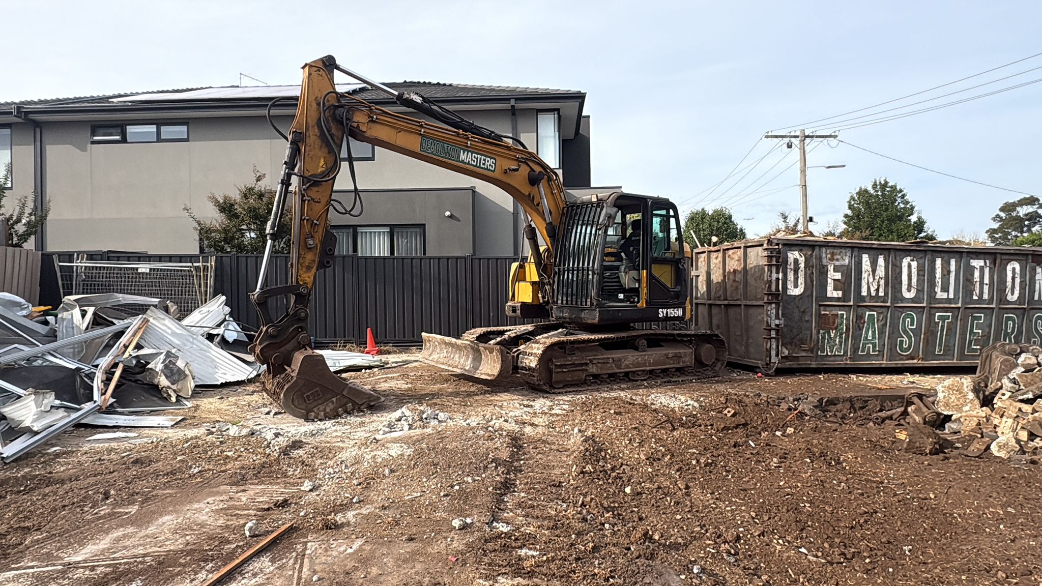 Demolition Masters branded skip bin and yellow excavator on a residential demolition site